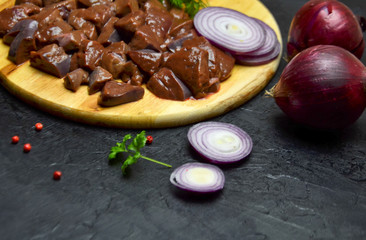 fresh chunks of beef liver on a cutting Board next to onions and spices on a wooden black table selective