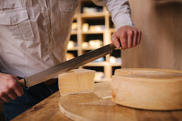 Man slicing a cheese on wooden board. Cheese shop