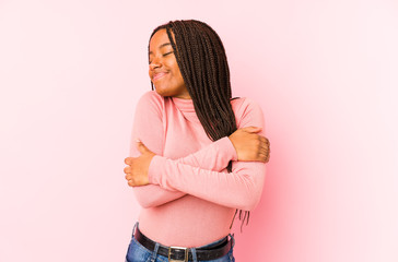 Young african american woman isolated on a pink background hugs, smiling carefree and happy.