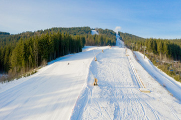 Aerial view of landscape of ski and snowboard slopes through pine trees going down to winter resort in Carpathians