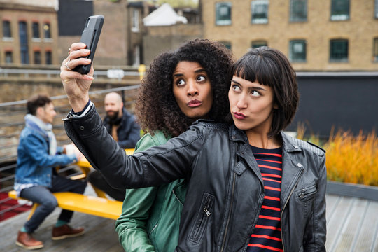 Portrait of Women on rooftop patio taking selfies with cell phone, East London, Great Britian