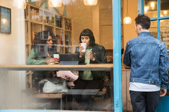 Two women sitting in window of cafe looking at tablet, East London, Great Britian