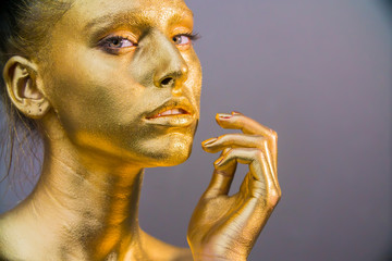 woman golden skin face in bright sparkles, Trendy glowing gold skin make-up. Glitter metallic shine makeup 