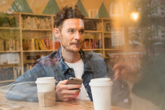 Friends sitting in window of cafe with mobile phone, East London, Great Britian