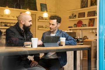 Friends sitting in window of cafe with tablet, East London, Great Britian