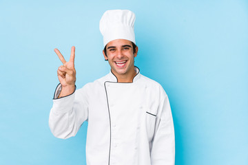 Young cook man isolated joyful and carefree showing a peace symbol with fingers.