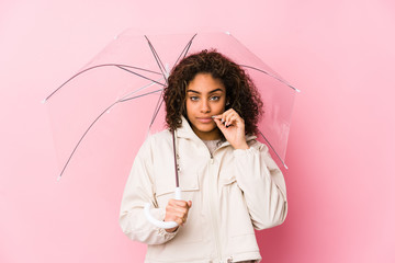 Young african american woman holding a umbrella with fingers on lips keeping a secret.