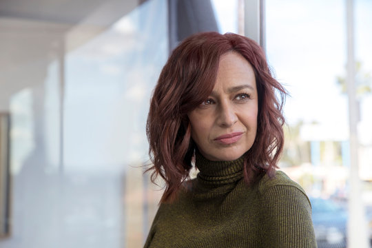 Mature woman with red hair, her back towards window, looks off frame., Studio City, CA, USA