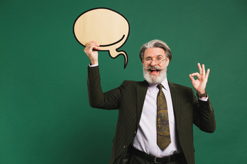Business middle-aged bearded man in khaki suit holding emoji with copy space and showing okay on a green background