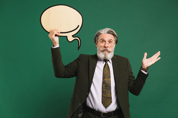 Business middle-aged bearded man in khaki suit holding emoji with copy space and waving a hand that does not know on a green background