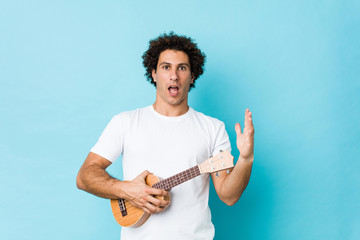 Young caucasian curly man playing ukelele celebrating a victory or success