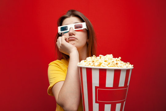 Sad Young Girl Watching A Bad, Boring Movie In 3d Glasses And With Popcorn On A Red Background