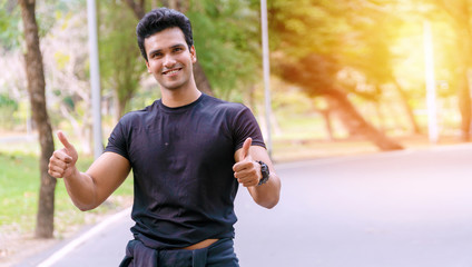 Handsome young man athletes showing positive thumbs up while standing or resting after exercising in the public park. Joyful athletic man showing thumbs up after workout for good healthy.