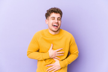 Young blond curly hair caucasian man isolated laughs happily and has fun keeping hands on stomach.