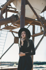 A long haired blonde woman, dressed all in black, wearing a black fedora type hat, black sun...
