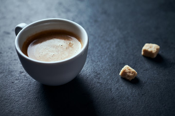 Cup of coffee and two brown sugar cubes on dark stone background. Close up.