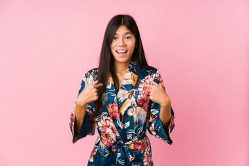 Young asian woman wearing a kimono pajamas surprised pointing with finger, smiling broadly.