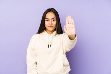 Young woman isolated on a purple background standing with outstretched hand showing stop sign, preventing you.