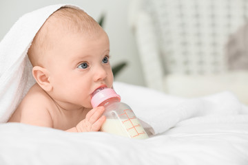 Portrait of cute little baby drinking milk from bottle on bed