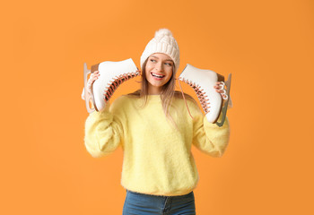 Beautiful young woman with ice skates on color background