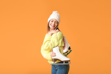 Beautiful young woman with ice skates on color background