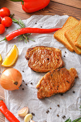 Tasty cooked pork steaks with bread and vegetables on table