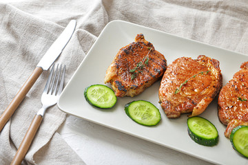 Plate with cooked pork steaks and cucumber on table