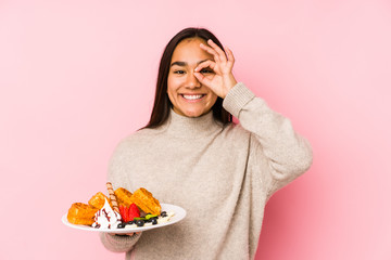 Young asian woman holding a waffle isolated excited keeping ok gesture on eye.