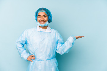 Young surgeon asian woman isolated showing a copy space on a palm and holding another hand on waist.