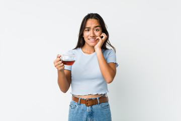 Young mixed race indian holding a tea cup biting fingernails, nervous and very anxious.