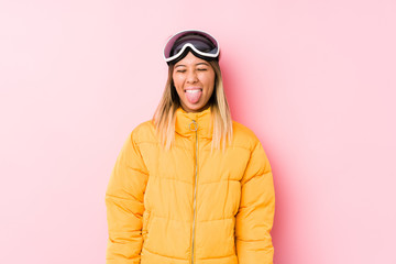 Young caucasian woman wearing a ski clothes in a pink background funny and friendly sticking out tongue.