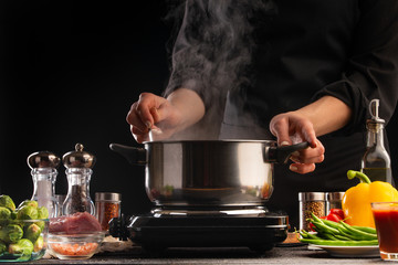 Culinary specialist or chef cooks soup or Italian pasta, from dressing. Heating a pan with steam, against a background of vegetables
