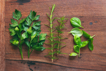 Fresh garden herbs, rosemary, basil and parsley on a rustic timber chopping block in authentic flat...