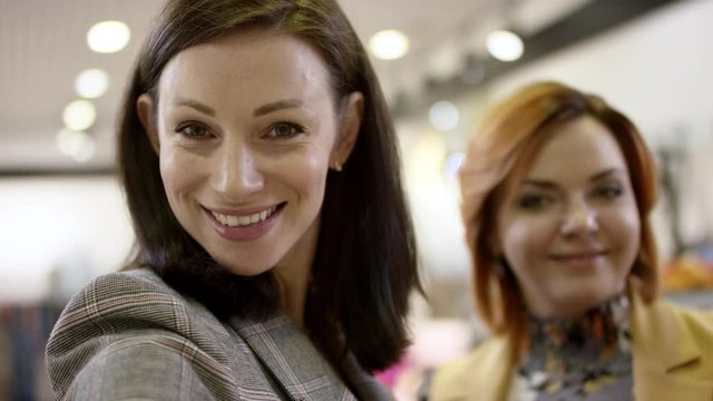 Two happy women are looking to the camera at the clothing store at mall and smling