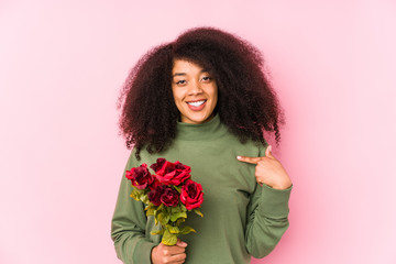 Young afro woman holding a roses isolated Young afro woman holding a rosesperson pointing by hand to a shirt copy space, proud and confident