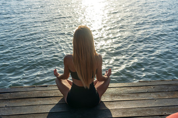 Silhouette of woman sitting at yoga pose on the tropical beach during sunset. Girl practicing yoga near sea water