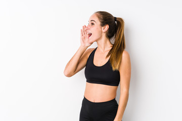 Young caucasian fitness woman posing in a white background shouting and holding palm near opened mouth.