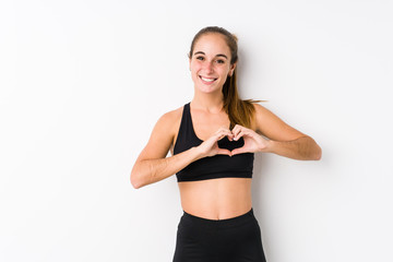Fototapeta premium Young caucasian fitness woman posing in a white background smiling and showing a heart shape with hands.