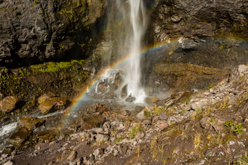 Fototapeta premium Rainbow Spans Across Base of Waterfall