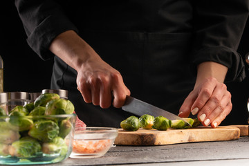 Cooking salad or sauce by a cook. Cutting brussels sprouts. On a black background, horizontal photo. Advertising, cooking, recipe book, home meals, restaurant business.