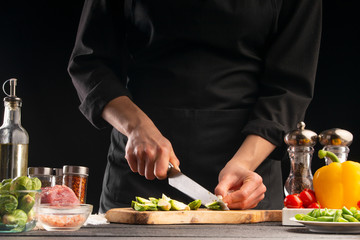 Cooking salad or sauce by a cook. Cutting brussels sprouts. On a black background, horizontal photo. Advertising, cooking, recipe book, home meals, restaurant business.