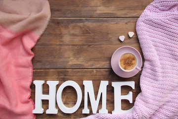 cappuccino with cinnamon in a pink cup, a gift in a box, sweets, candles, cones, plaid on an old wooden table, the word home, top view, flat, concept cozy home, copy space