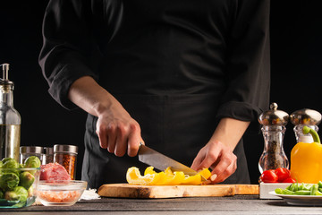 Chef gotomit salad, slicing peppers on a background with vegetables. Ingredients for cooking. Restaurant business, cooking, tasty and healthy nutrition.