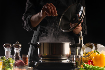 Culinary specialist or chef cooks soup or Italian pasta, from dressing. Heating a pan with steam, against a background of vegetables. Recipe book, cooking, gastronomy, freezing in motion.
