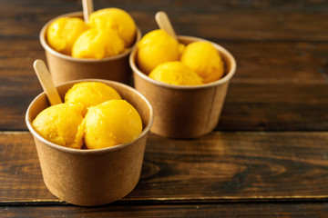 Three paper cups with mango sorbet on rustic background