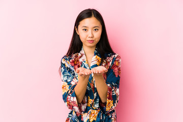 Young chinese woman wearing a kimono pajama isolated holding something with palms, offering to camera.