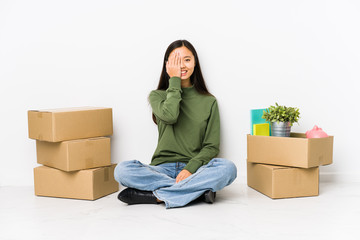 Young chinese woman moving to a new home having fun covering half of face with palm.