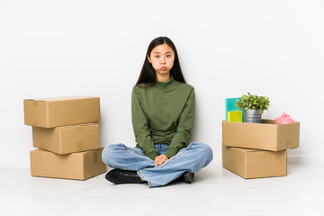 Young chinese woman moving to a new home blows cheeks, has tired expression. Facial expression concept.