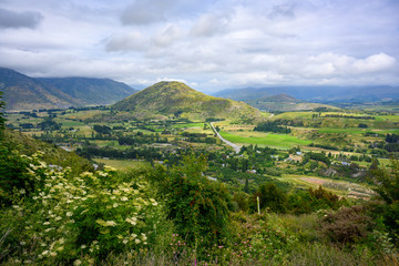 Arrow Junction Lookout point, a mountain viewpoint overlooking mountains and villages. In the summer, there are wild flowers and green fields at Crown Range Road, Otago, New Zealand.