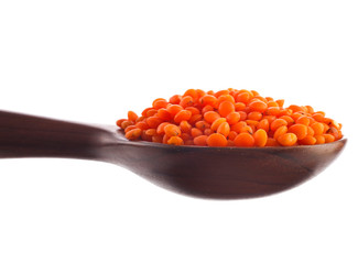 Red lentils in the wooden spoon isolated on a white background.